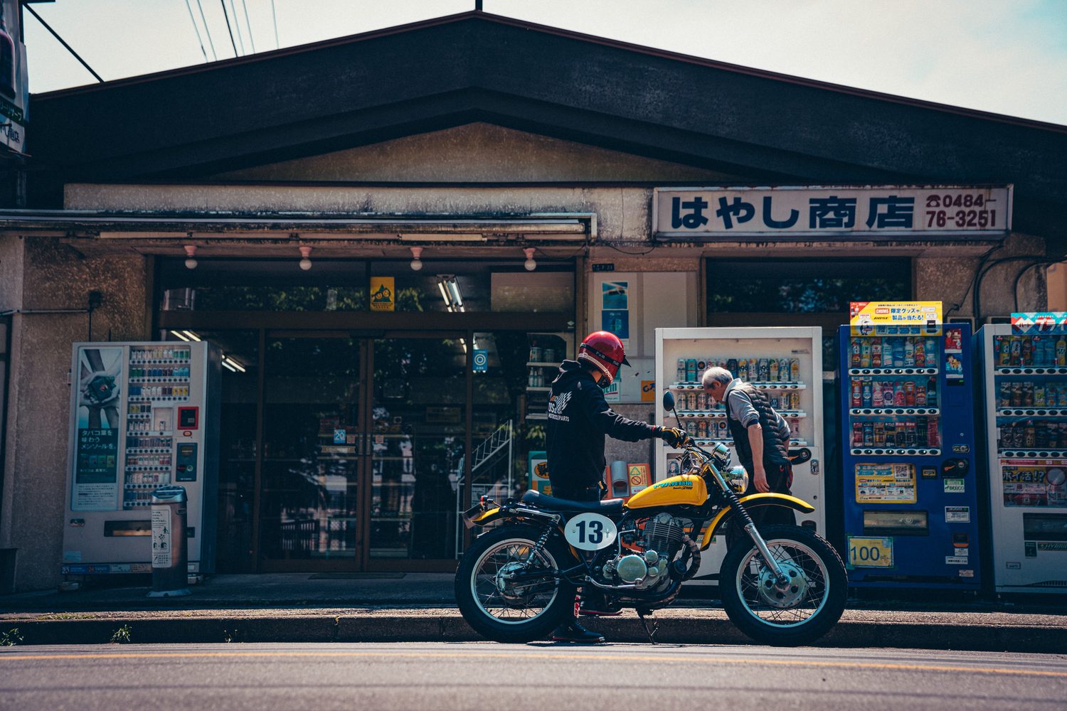昔ながらの商店の前で、SR400とともに店の人と話すライダー